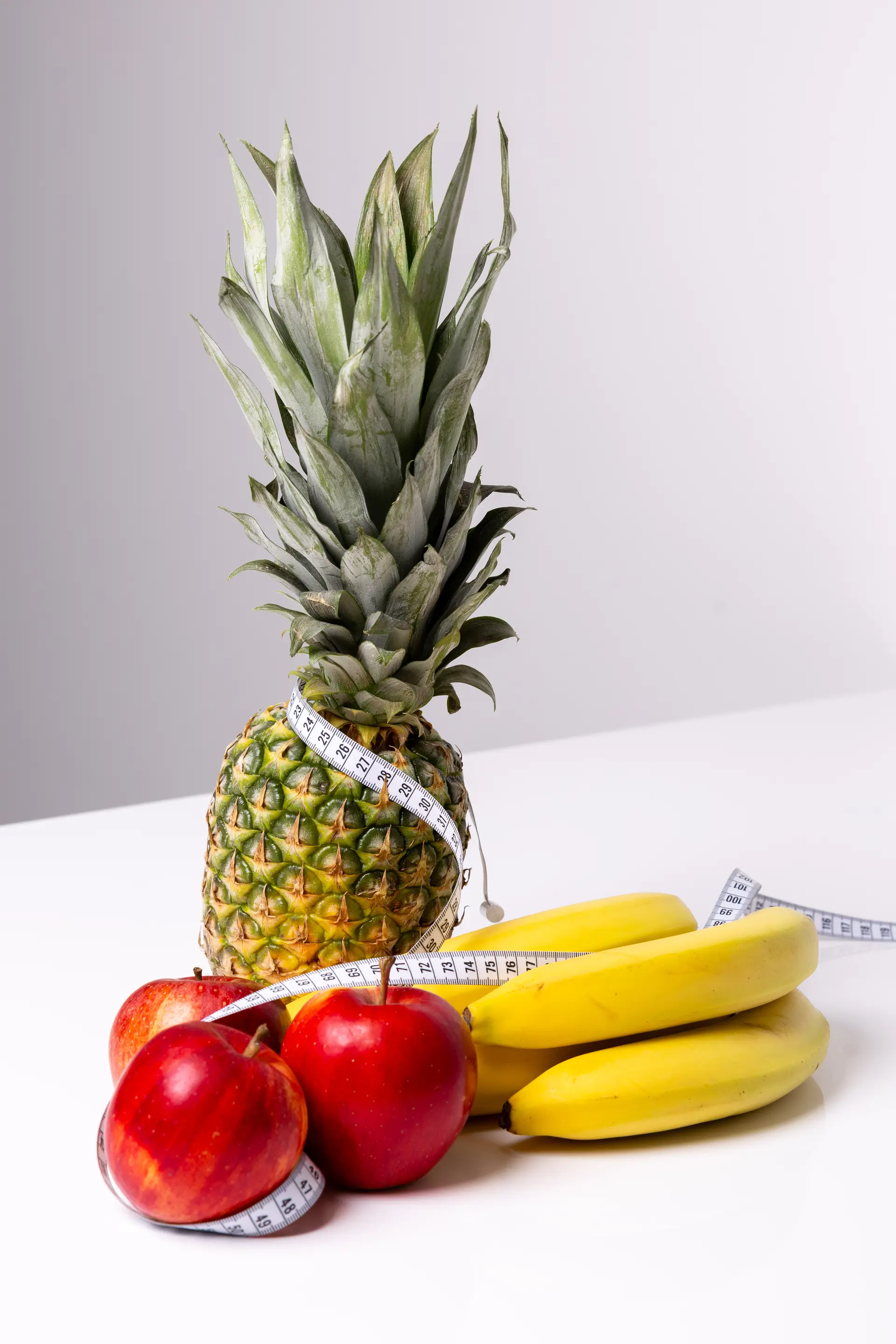 Ananas, jabłka i banany przewiązane centymetrem krawieckim